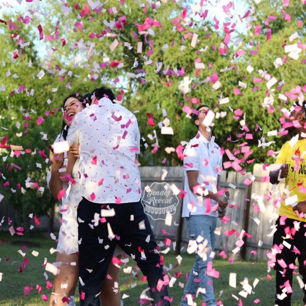 Couple hugging joyfully as they are showered with pink gender reveal confetti cannons