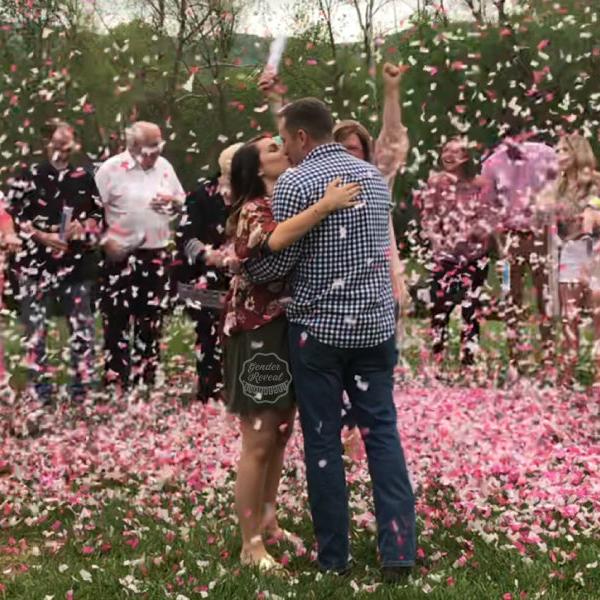 A couple kissing, while their friends and family fire off pink confetti cannons all around them.